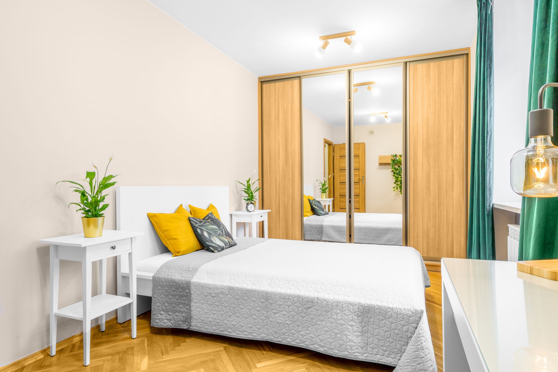 Compact bright bedroom with a gray bed, mirrored wardrobe, small table and green curtains