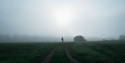 Free A lone figure on a dirt road through a misty field, with a barn in sight. Stock Photo