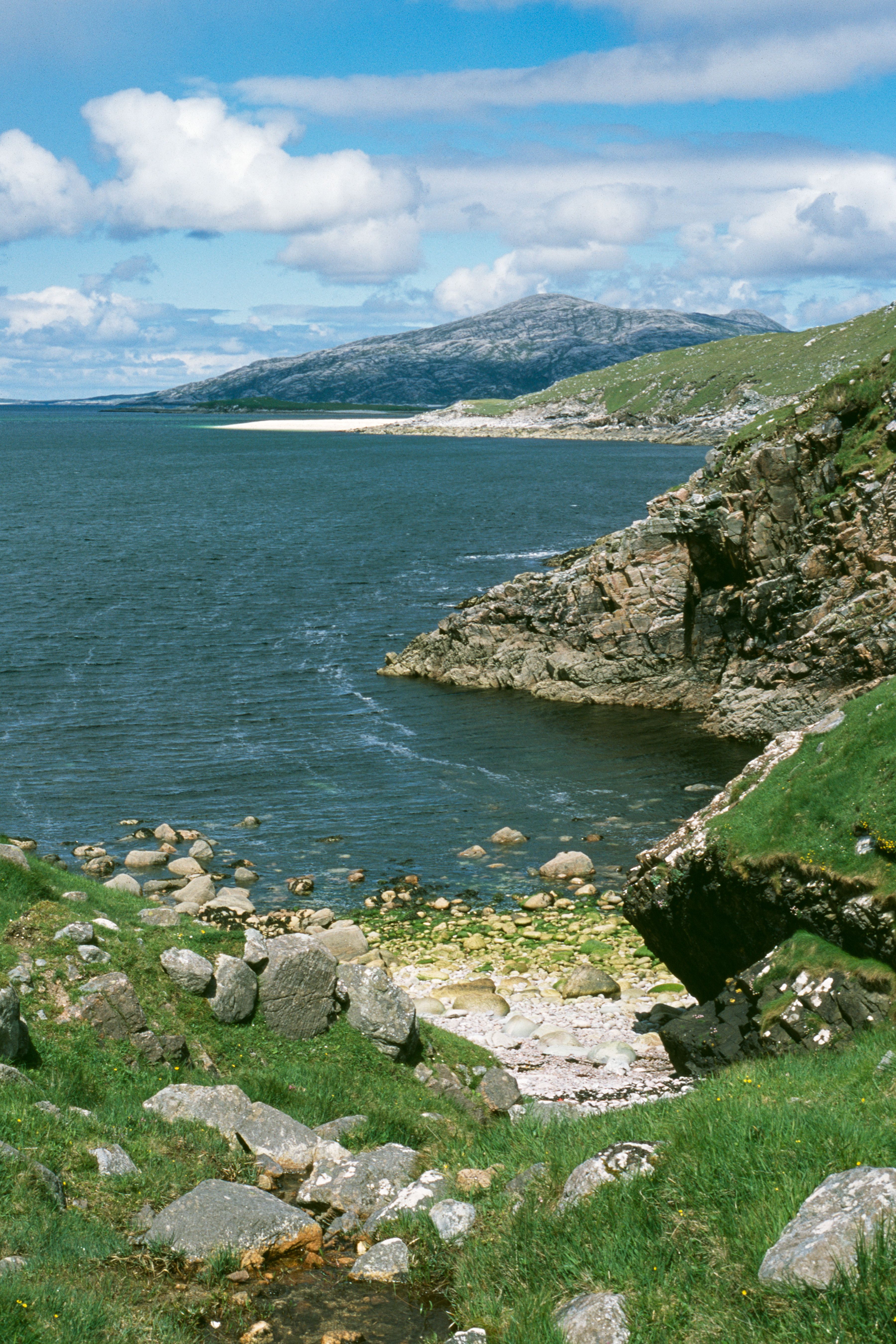 Scenic view of a rocky coast with hills and sea under a cloudy sky.
