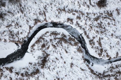 Aerial View of a Curved River Between Snow Covered Ground