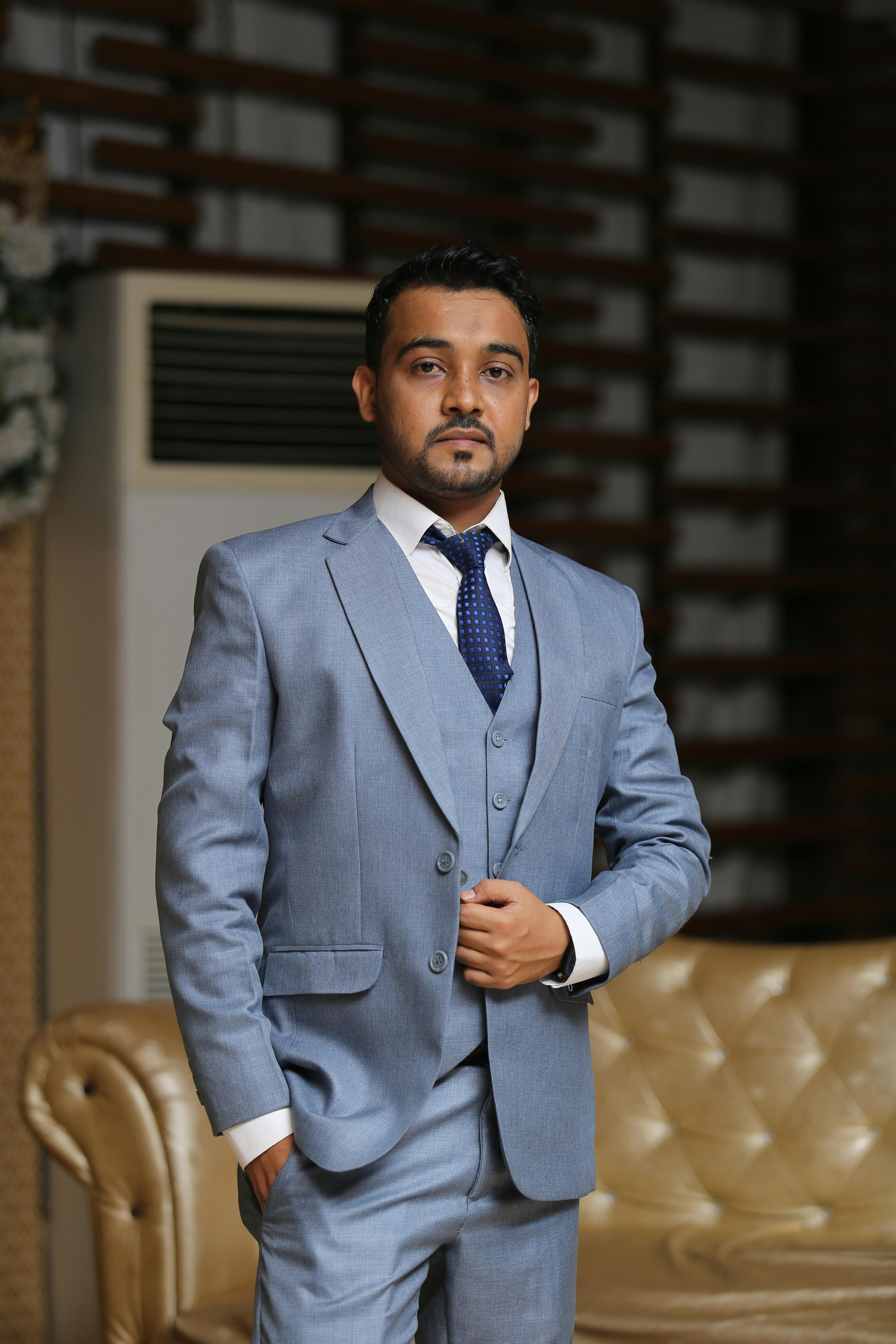 A confident man in a blue suit posing indoors with a sophisticated look.