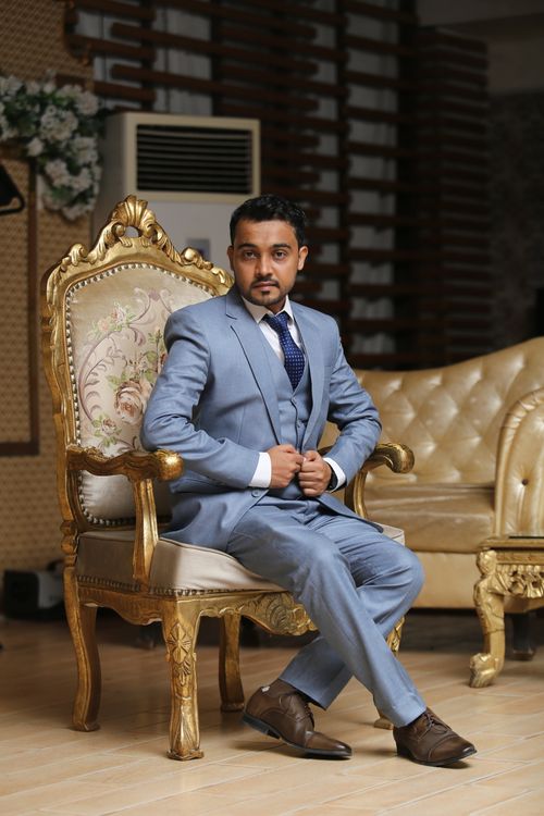 Free A stylish man in a blue suit poses elegantly indoors on a luxurious chair. Stock Photo