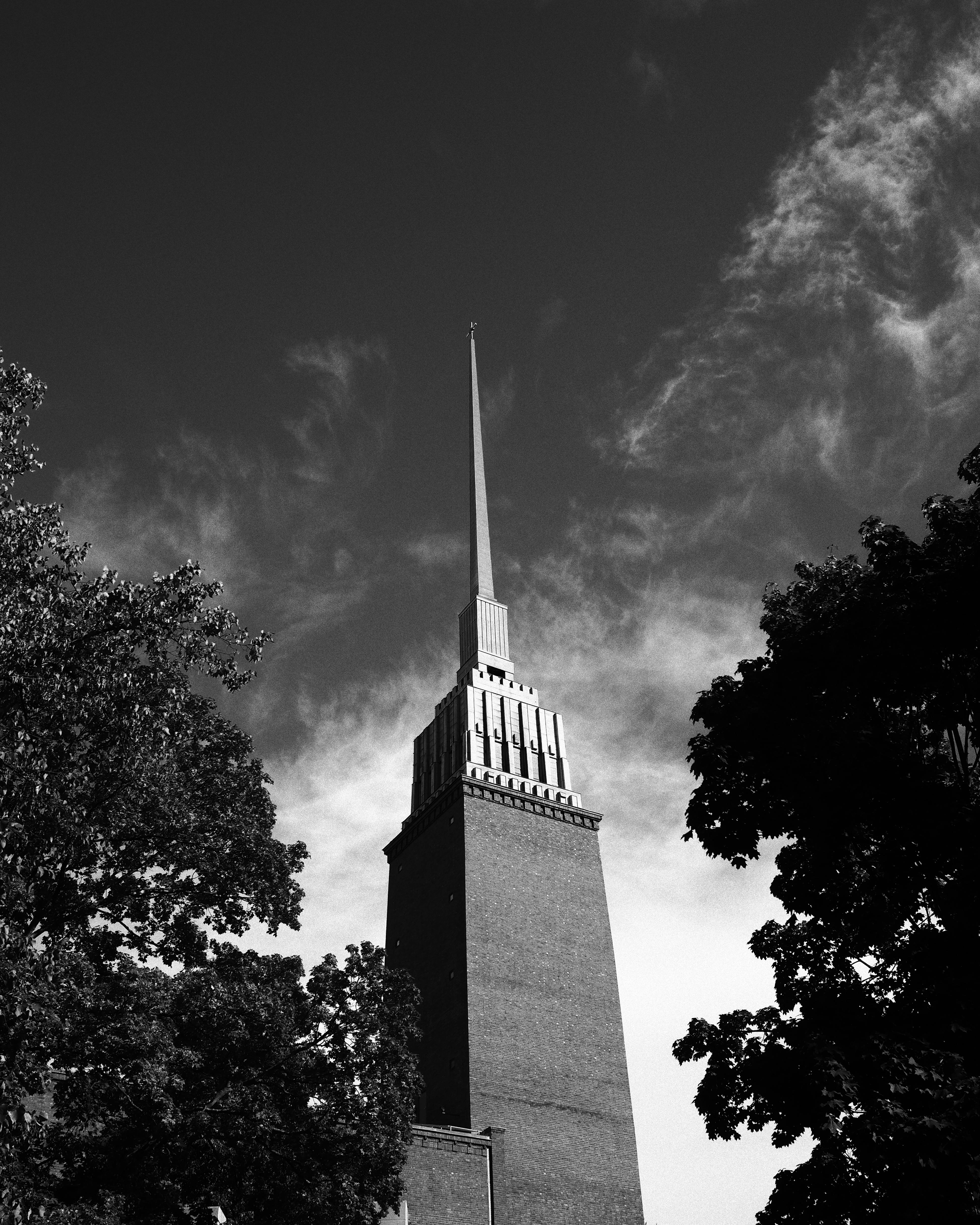 Striking black and white photo of a Helsinki tower set against a dramatic sky, surrounded by trees.