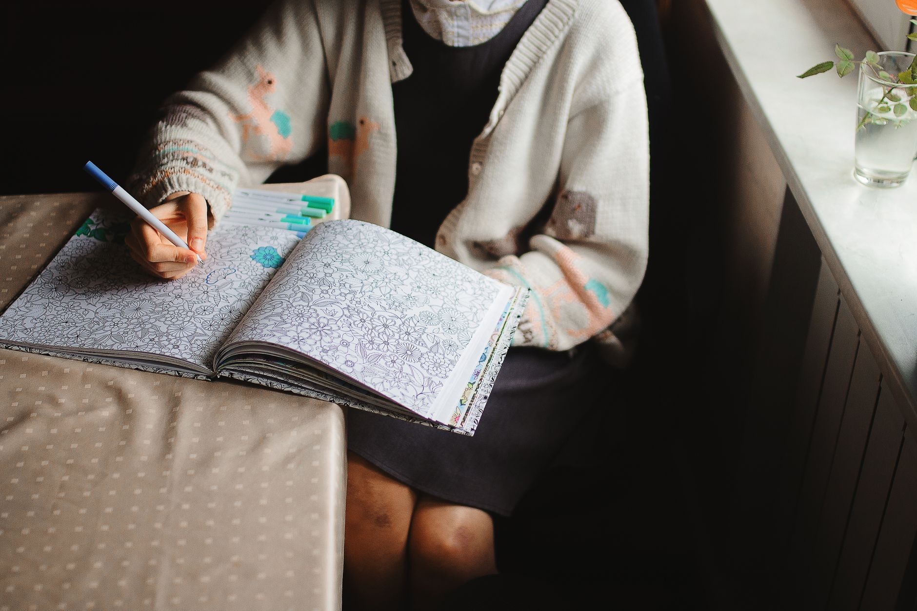 Adult woman coloring intricate designs in a book by a window
