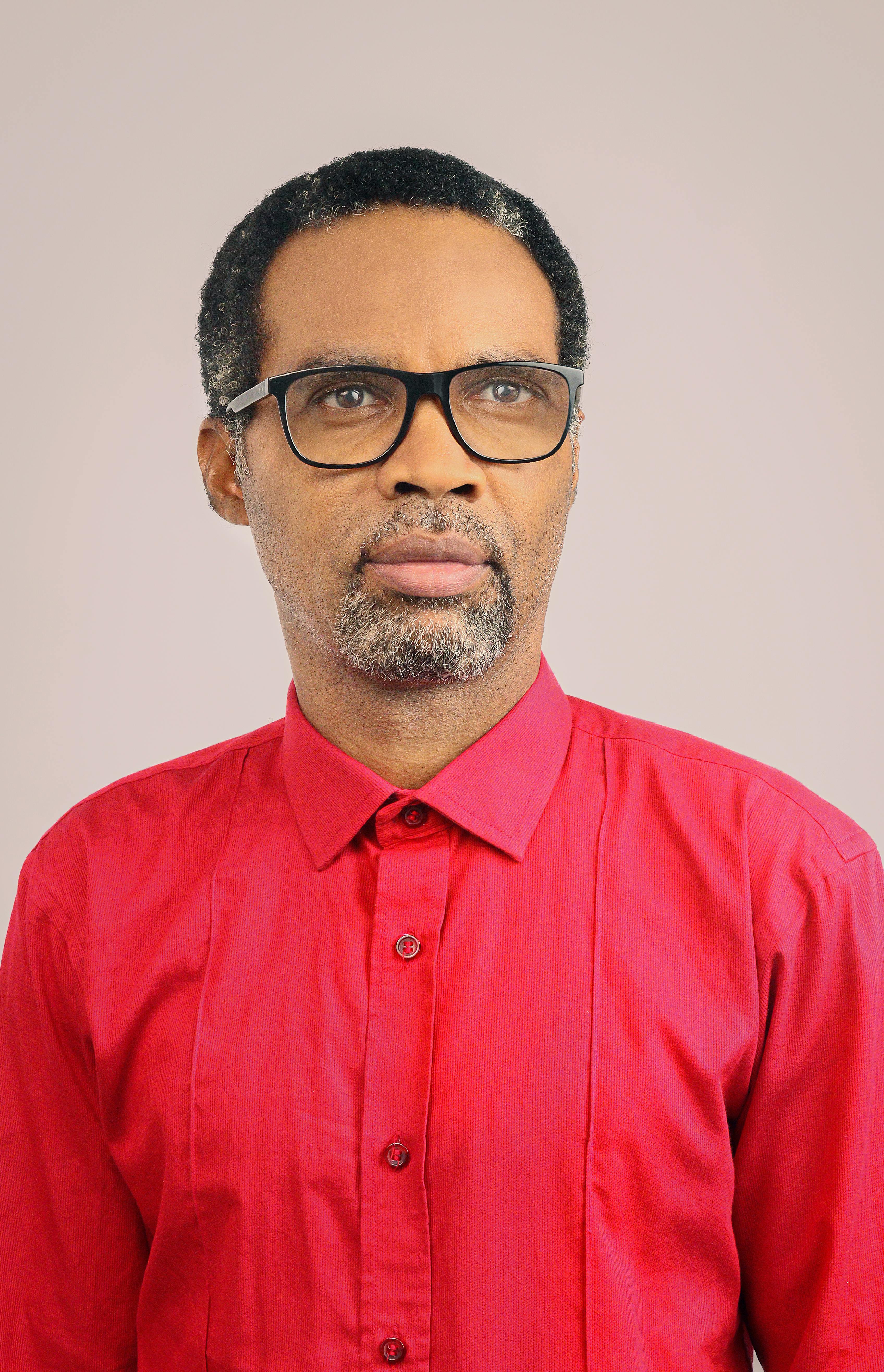 Studio portrait of an adult man wearing glasses and a red shirt.