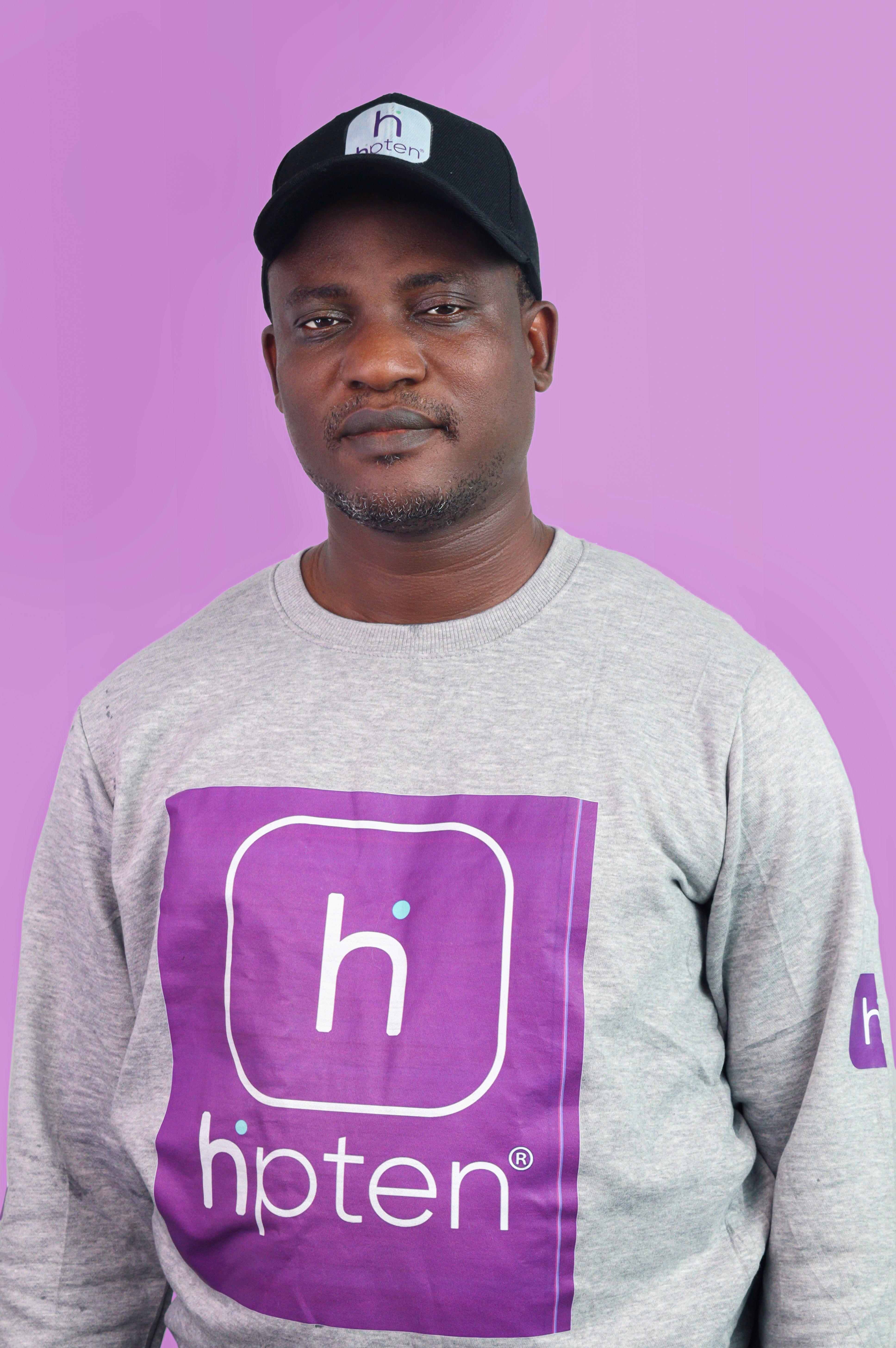 Man wearing branded cap and shirt poses against a purple background.