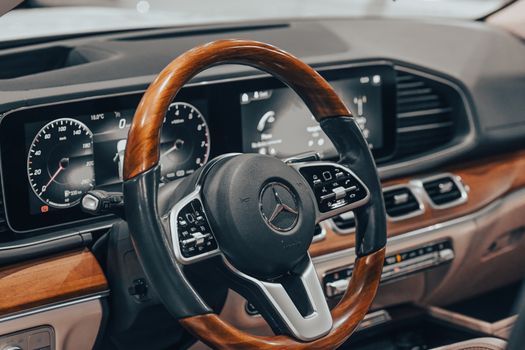 Close-up of a luxury car interior featuring a wooden steering wheel and digital dashboard displays.