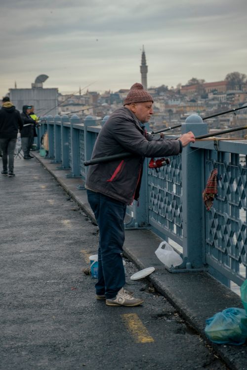 Free A man enjoys fishing on a bustling urban bridge with the city skyline in the background. Stock Photo