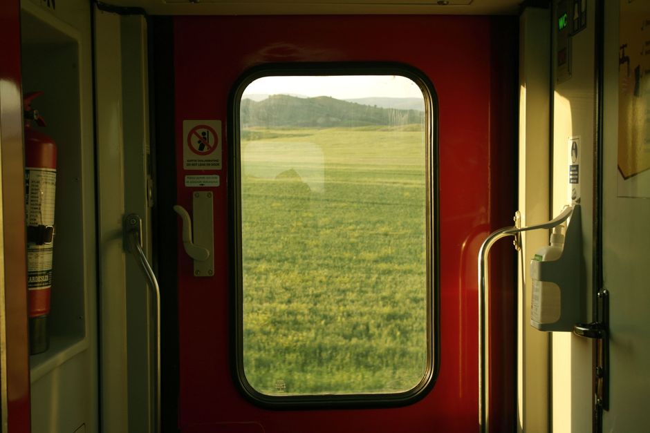 View of green fields through a train window with red interior lighting.
