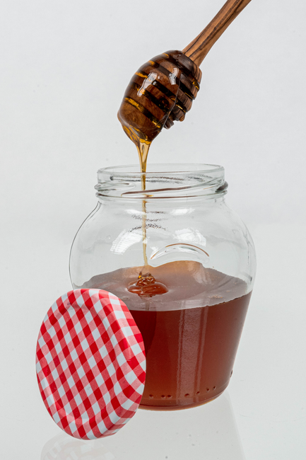 Close-up of honey pouring from a dipper into a glass jar with a red checkered lid, isolated on white. - Expert Tips for Selecting Honey