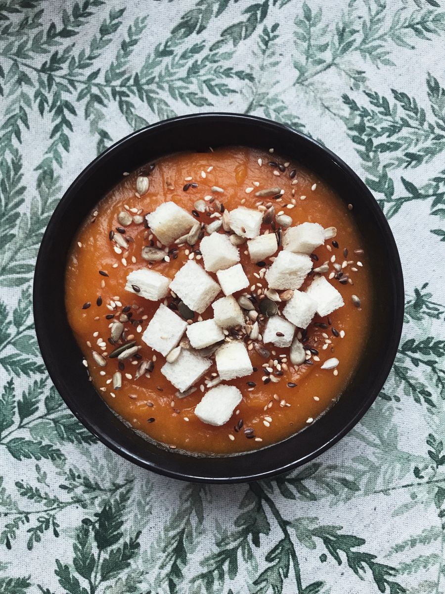 Top view of a creamy pumpkin soup garnished with croutons and seeds
