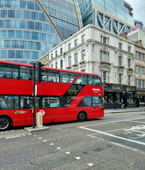 Iconic red double-decker bus on a busy London street with modern and historic buildings.