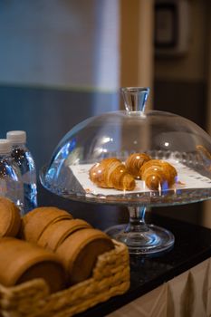 Golden croissants under a glass dome on a catering table.