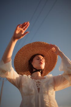 A woman in a white dress with a sun hat basks in the warm light of sunset.