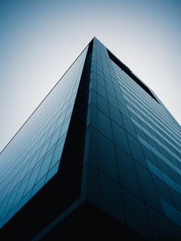 Dramatic low angle view of a sleek, modern skyscraper against a gradient blue sky.