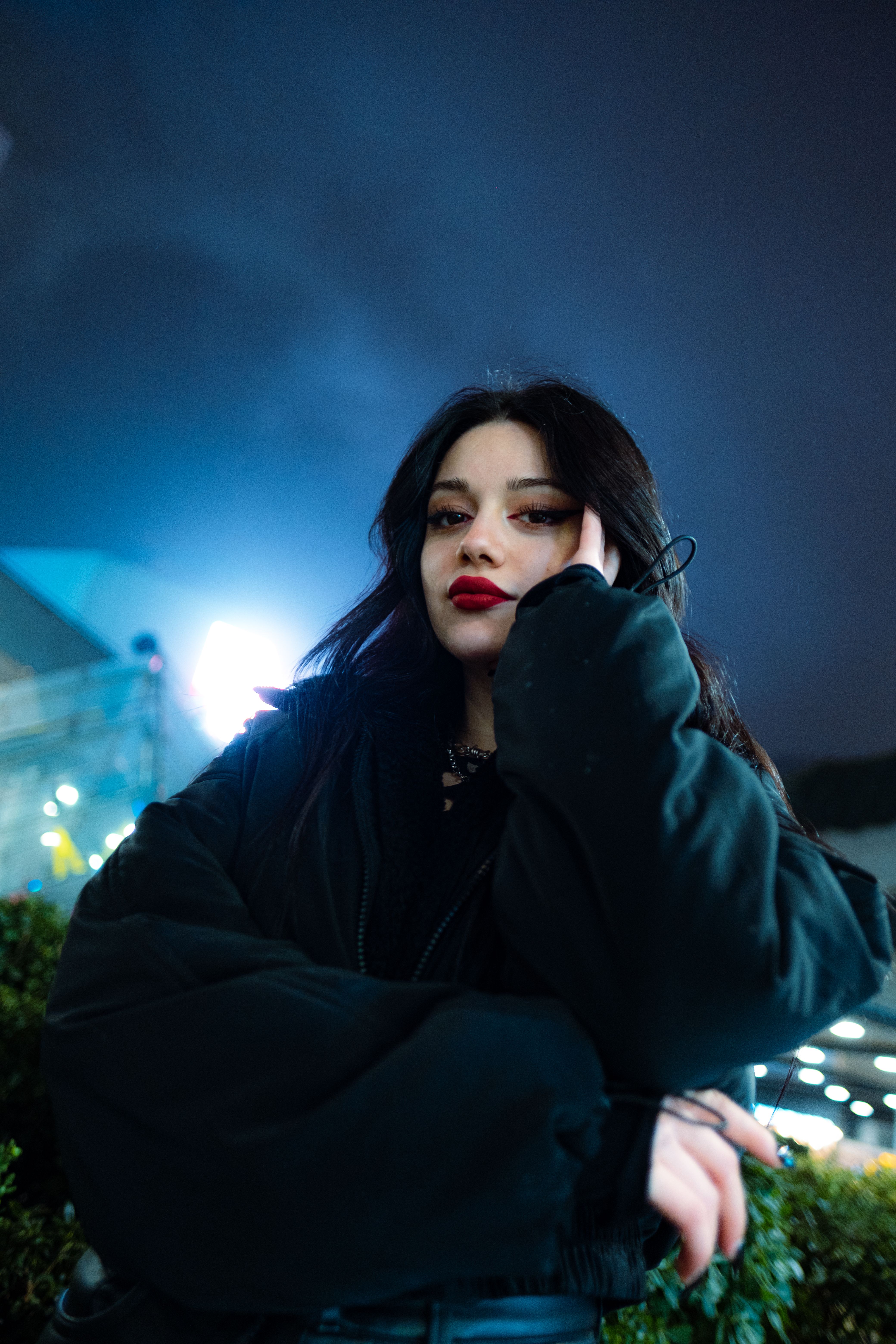 Captivating woman with red lips under city lights at night, exuding modern style.