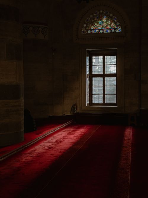 Free Moody interior view of an Istanbul mosque featuring a red carpet and stained glass window. Stock Photo
