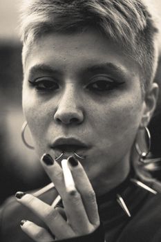 A moody black and white portrait of a young woman smoking with striking eyeliner and short hair.