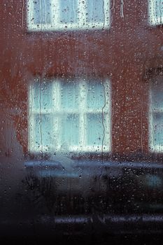 Moody view through a rain-soaked window with building in the blurred background.