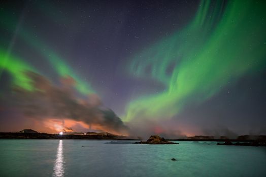 Capture of vibrant aurora borealis illuminating the night sky over Keflavík, Iceland's serene coastline.