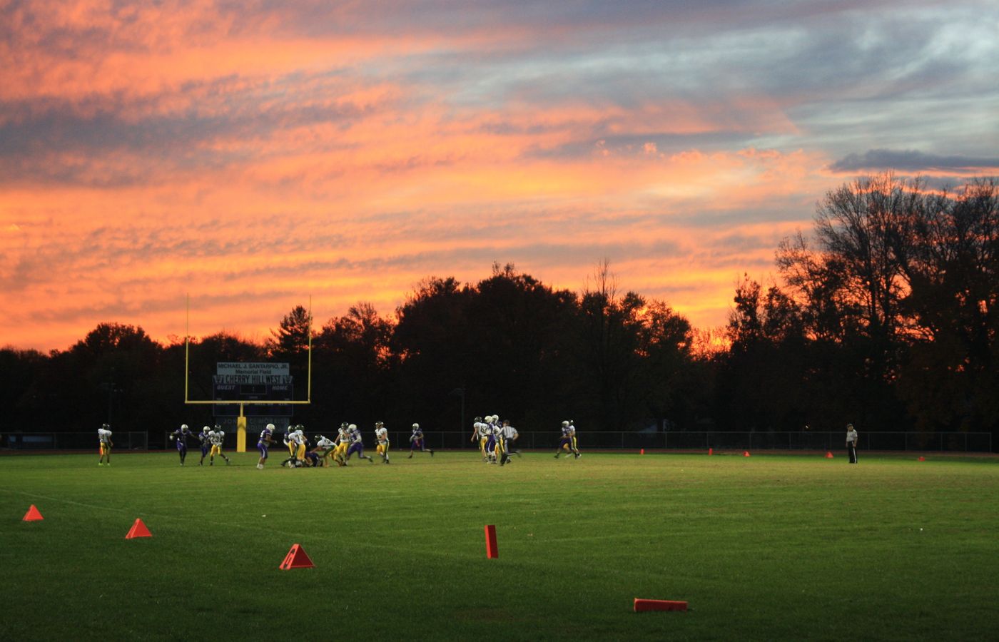 A vibrant sunset backdrop frames a football game on a green field, showcasing teamwork and competition.