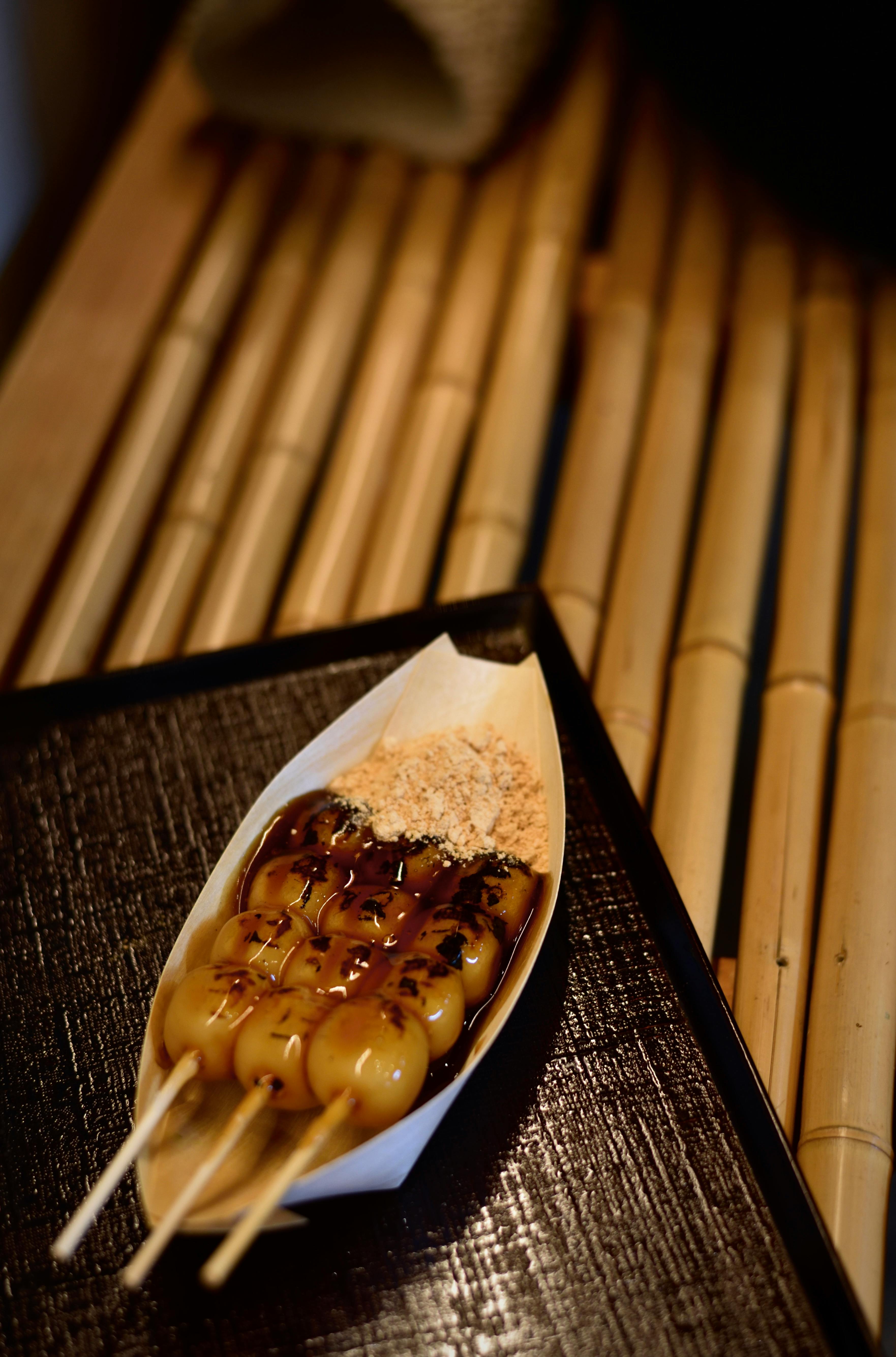 Close-up of traditional Japanese dango skewers glazed with sweet soy sauce, presented on a bamboo mat.