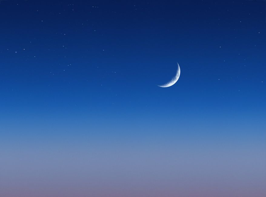 A serene view of a crescent moon against a deep blue sky speckled with stars.