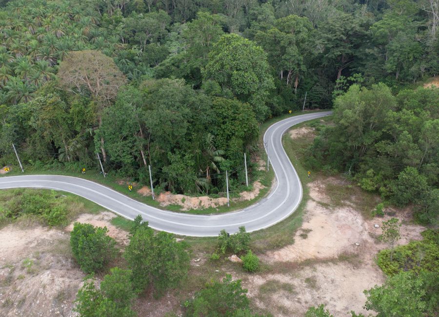 Aerial view of a winding road cutting through dense forest near Lumut, Malaysia.
