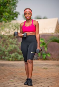 Confident woman in activewear lifting dumbbells outdoors, embracing fitness and healthy lifestyle.