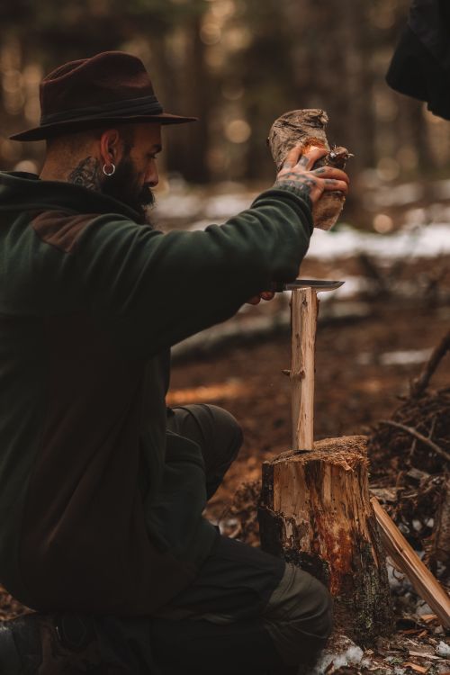 Free Adult man chopping wood with knife in forest, showcasing outdoor skills and preparation. Stock Photo