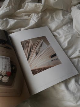 A serene close-up of an open magazine resting on a white bedspread, inviting relaxation.