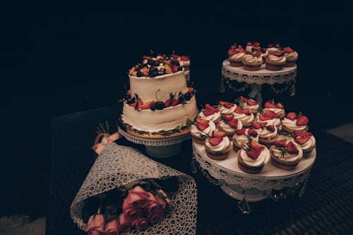 A Layer Cake, Cupcakes and a Bouquet of Roses on a Table 