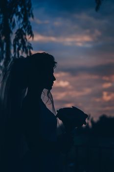 Elegant silhouette of a bride holding a bouquet against a stunning sunset backdrop, perfect for romantic themes.