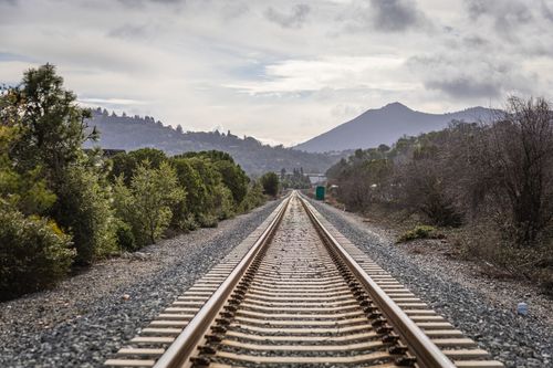 Free Railroad tracks extend into the horizon with hills and trees under an overcast sky. Stock Photo