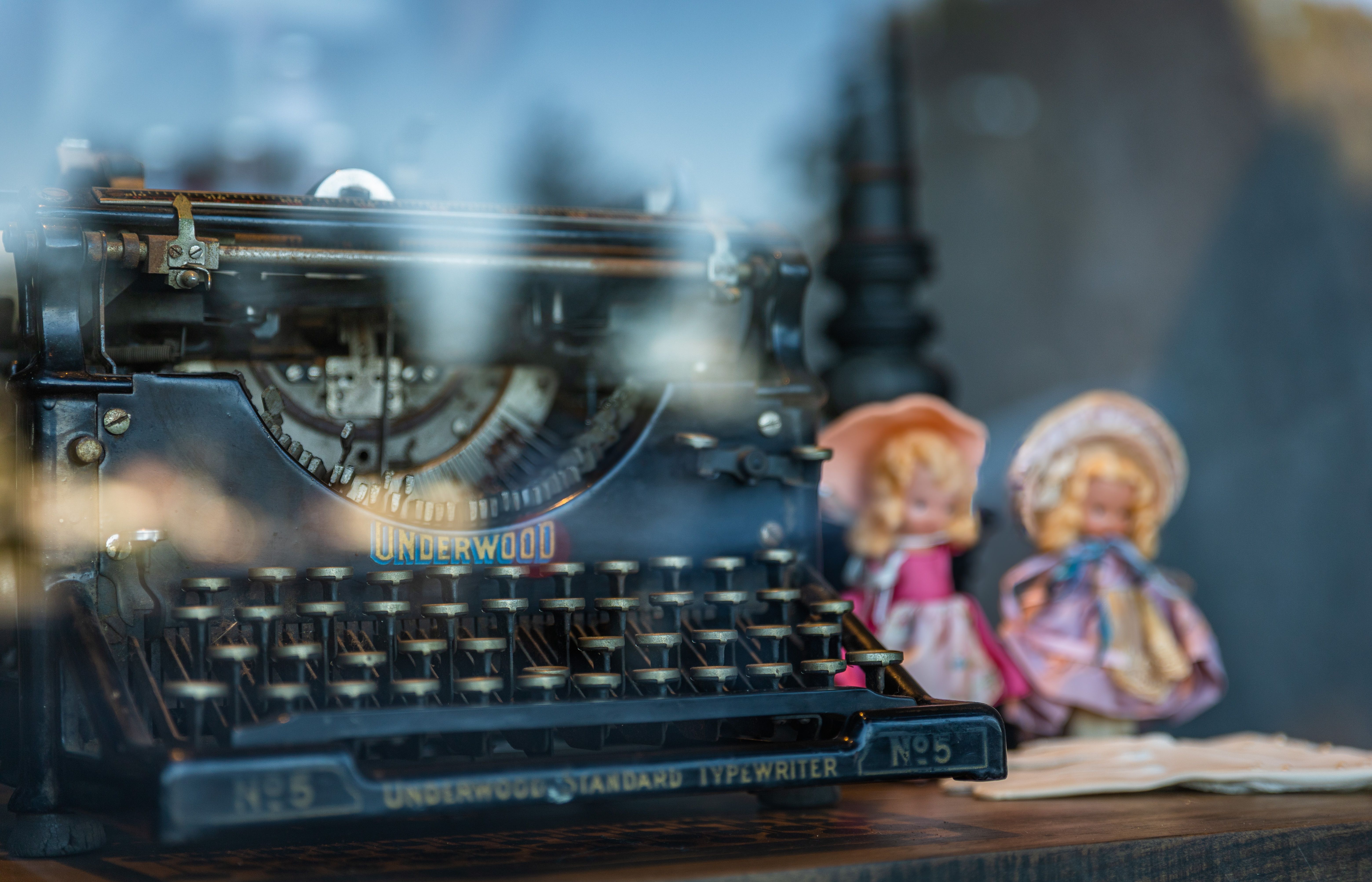 An antique Underwood typewriter with vintage dolls reflected in a window display, evoking the nostalgic literary atmosphere of 1920s Paris.