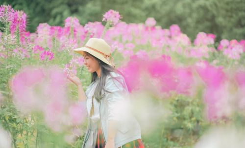 Free Asian woman in a straw hat admiring pink flowers in a vibrant field during daylight. Stock Photo