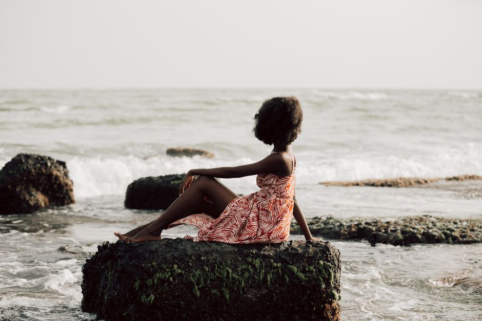 Woman in a summer dress sitting on a rock by the sea, enjoying a peaceful moment.