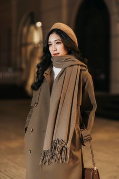 Elegantly dressed woman in warm winter attire standing in an urban setting at night.