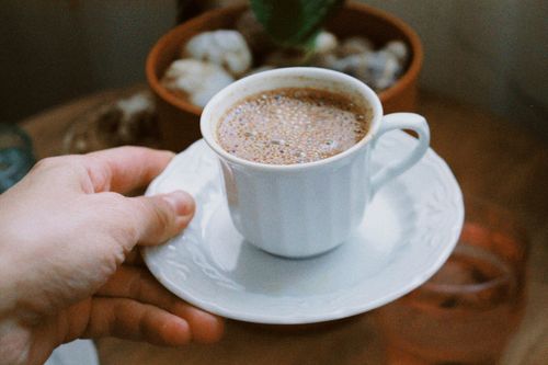 Free A close-up of a hand holding a traditional Turkish coffee cup with rich crema. Stock Photo