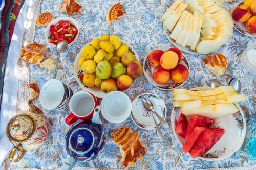 Free Bright picnic setup with diverse fruits, melons, and tea on an ornate tablecloth. Stock Photo