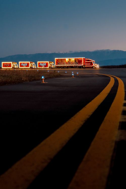 Free Illuminated trucks in a convoy on a curved highway during twilight, showcasing a festive scene. Stock Photo