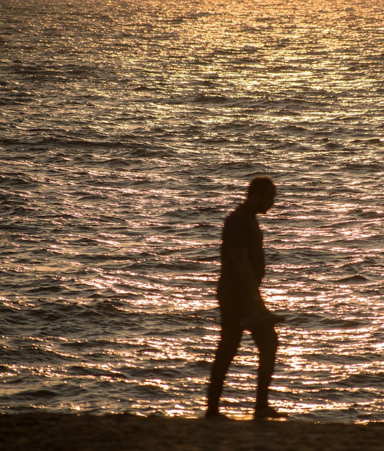 A Silhouette Of A Person Walking On The Beach