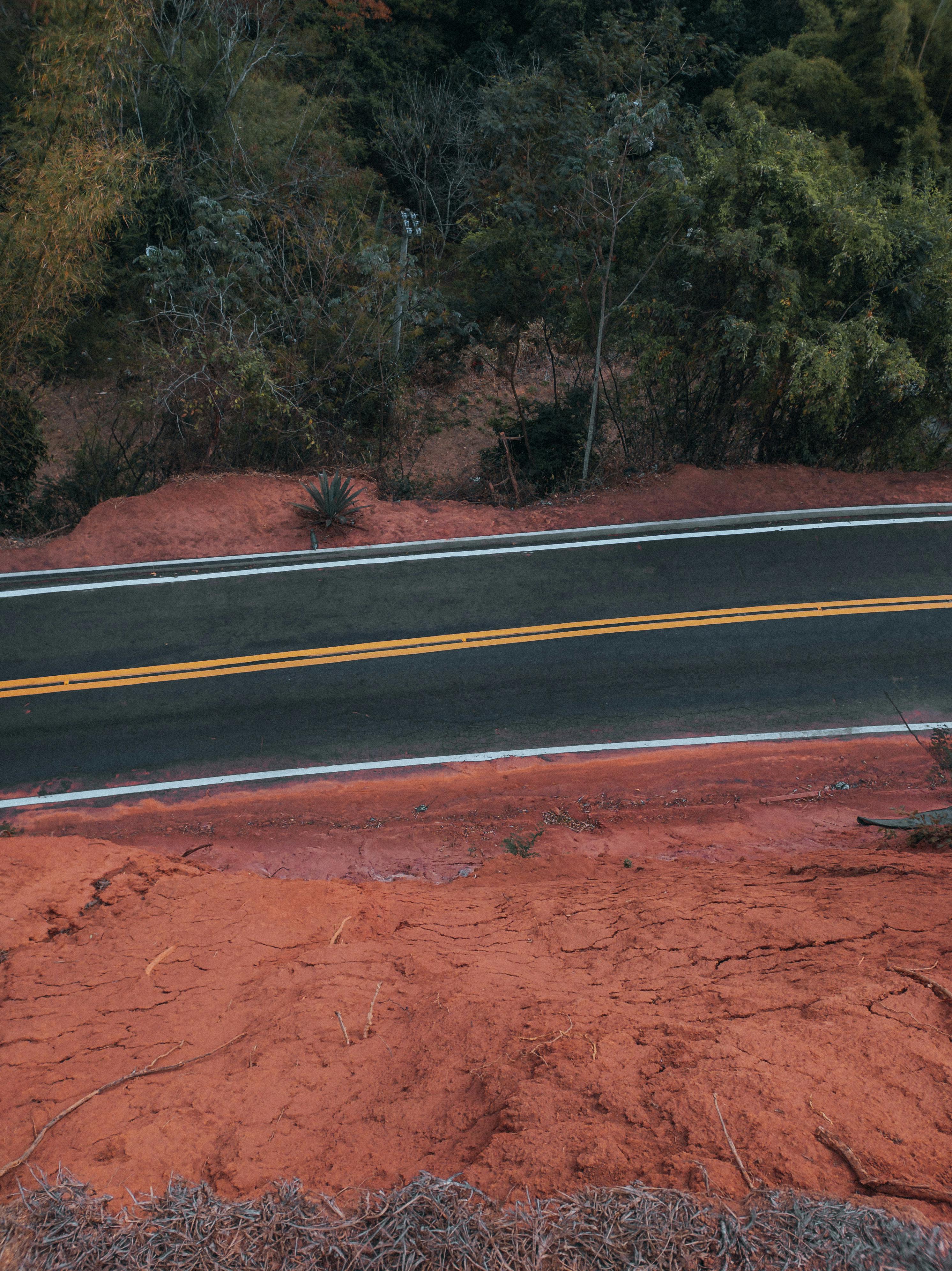 Captivating aerial view of a road cutting through vibrant red soil and lush greenery, showcasing nature's contrast.