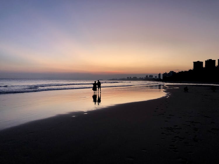 Silhouettes Of People Walking On A Beach At Sunset