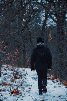A man in winter attire walks along a snow-covered path in a wooded area.