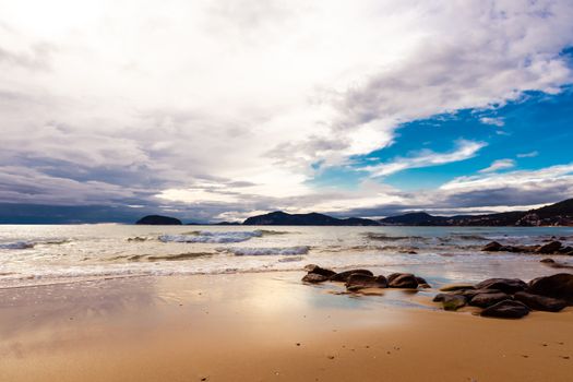 Serene beach scene in Xanthi, Greece, featuring a rocky shore and calm blue sea under a dramatic sky.