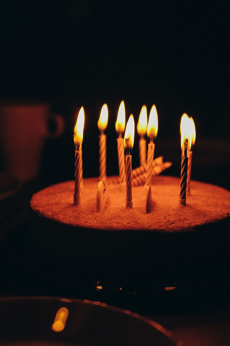 Vertical shot of a birthday cake with burning candles against a dark background, creating a warm ambiance.