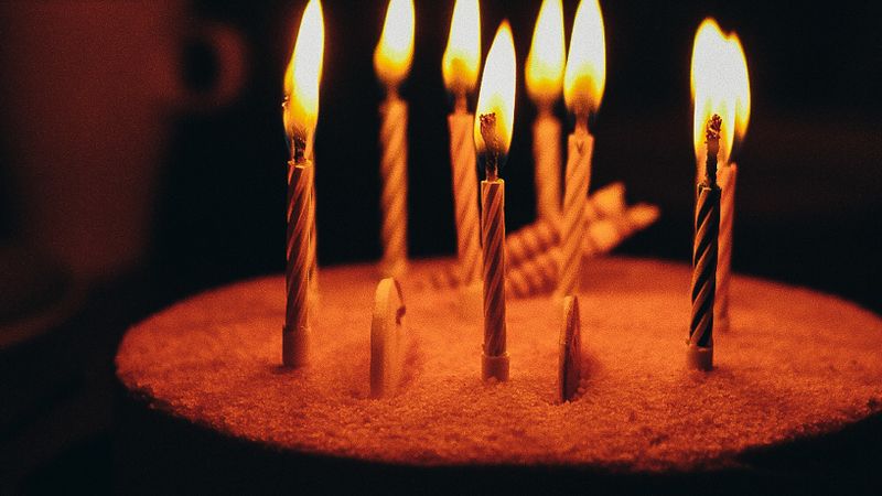 Vertical shot of a birthday cake with burning candles against a dark background, creating a warm ambiance.
