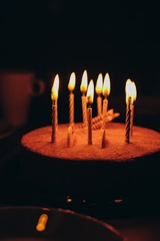 Vertical shot of a birthday cake with burning candles against a dark background, creating a warm ambiance.
