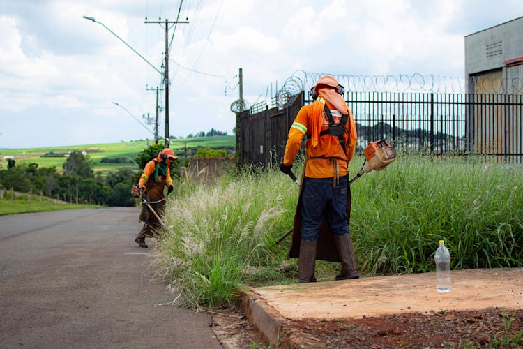 Workers Cutting Grasses On The Side Of The Road Near Metal Gate